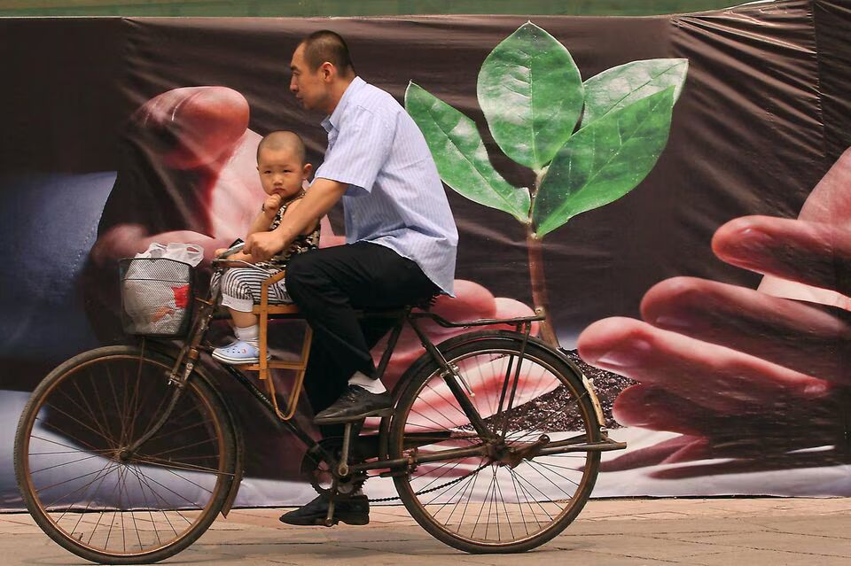 Ein Mann mit Kleinkind radelt an einem Plakat vorbei, das schon 2010 für die grüne Wende in China warb © IMAGO